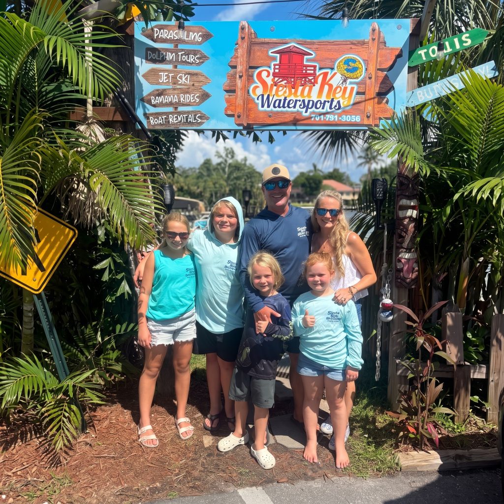 The Siesta Key Watersports team and family smiling together under the business signage in Sarasota, Florida.